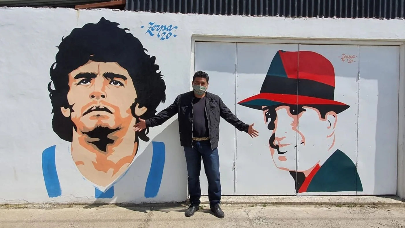 Benito Zerpa, posa junto a sus dos obras impresas en el muro de su casa.
