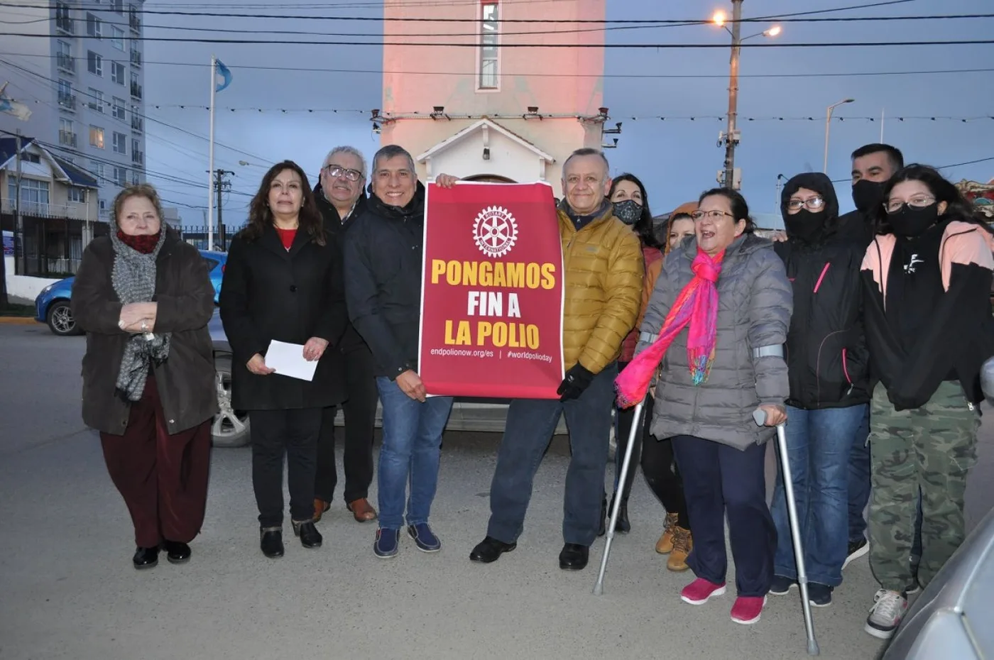 Integrantes del Rotary club Isla Grande frente a la torre iluminada de rojo con la consigna "Pongamos fin a la polio".