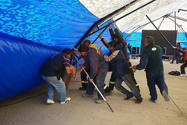 Un grupo de personas intenta apuntalar una de las guías metálicas de la carpa.