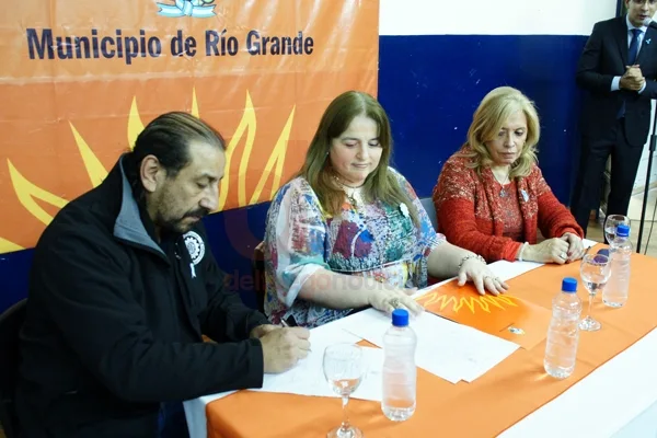 Martínez firma el convenio; lo observan Castillo y Muñoz.